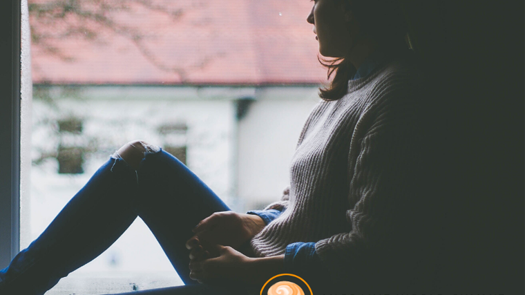 Migraine World Summit logo imposed on a background showing a silhouette of a woman sitting on a windowsill staring outside